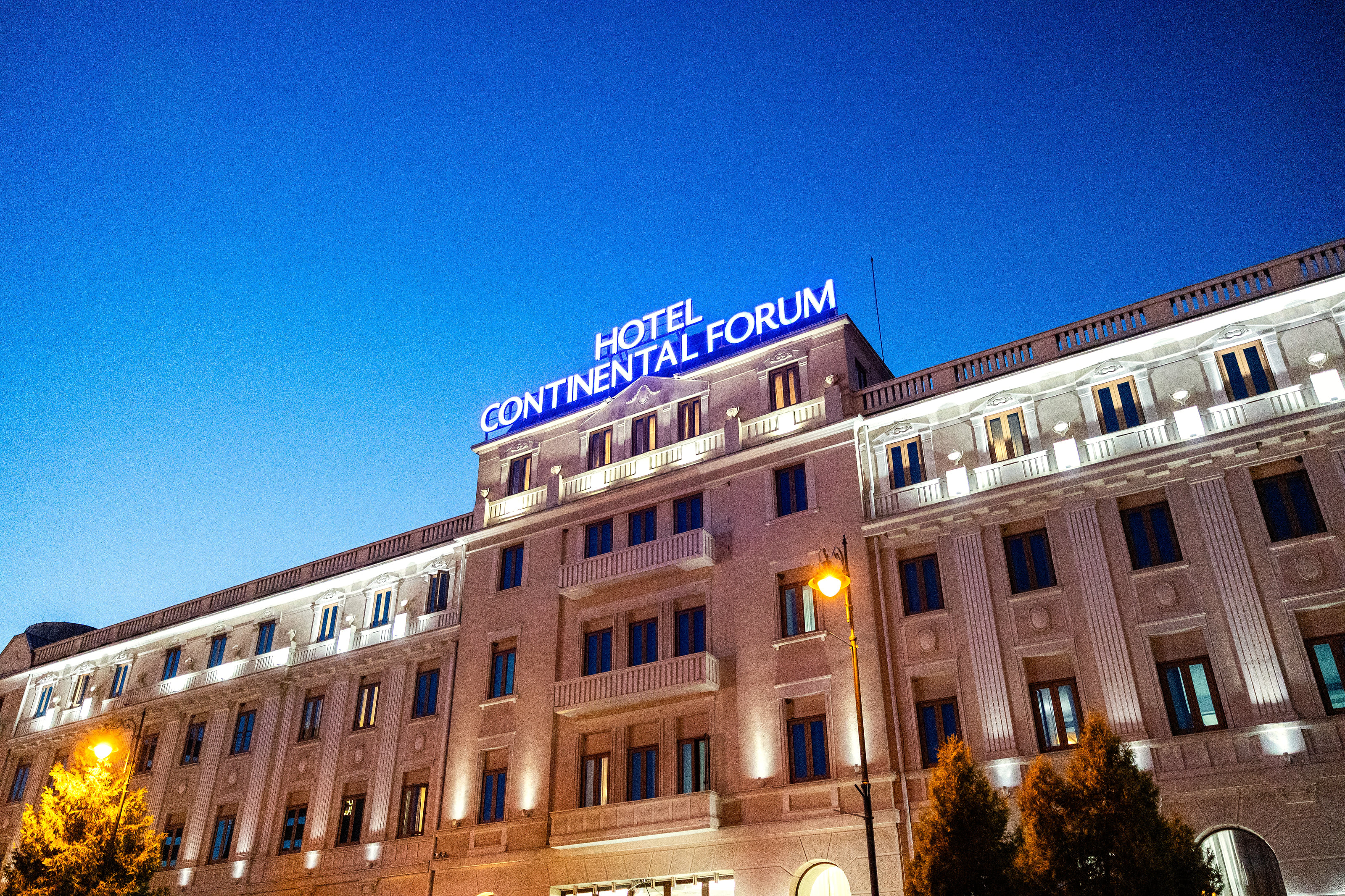 Hotel Continental Forum in Sibiu at night: a long, lit facade with balconies and the hotel's name on the roof.
